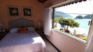 Un dormitorio con cama, mesita de noche y ventana con vista a una playa y barcos.