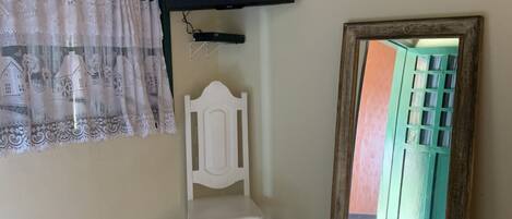 A room with a bed, a white chair, a TV mounted on the wall, and a window with curtains.