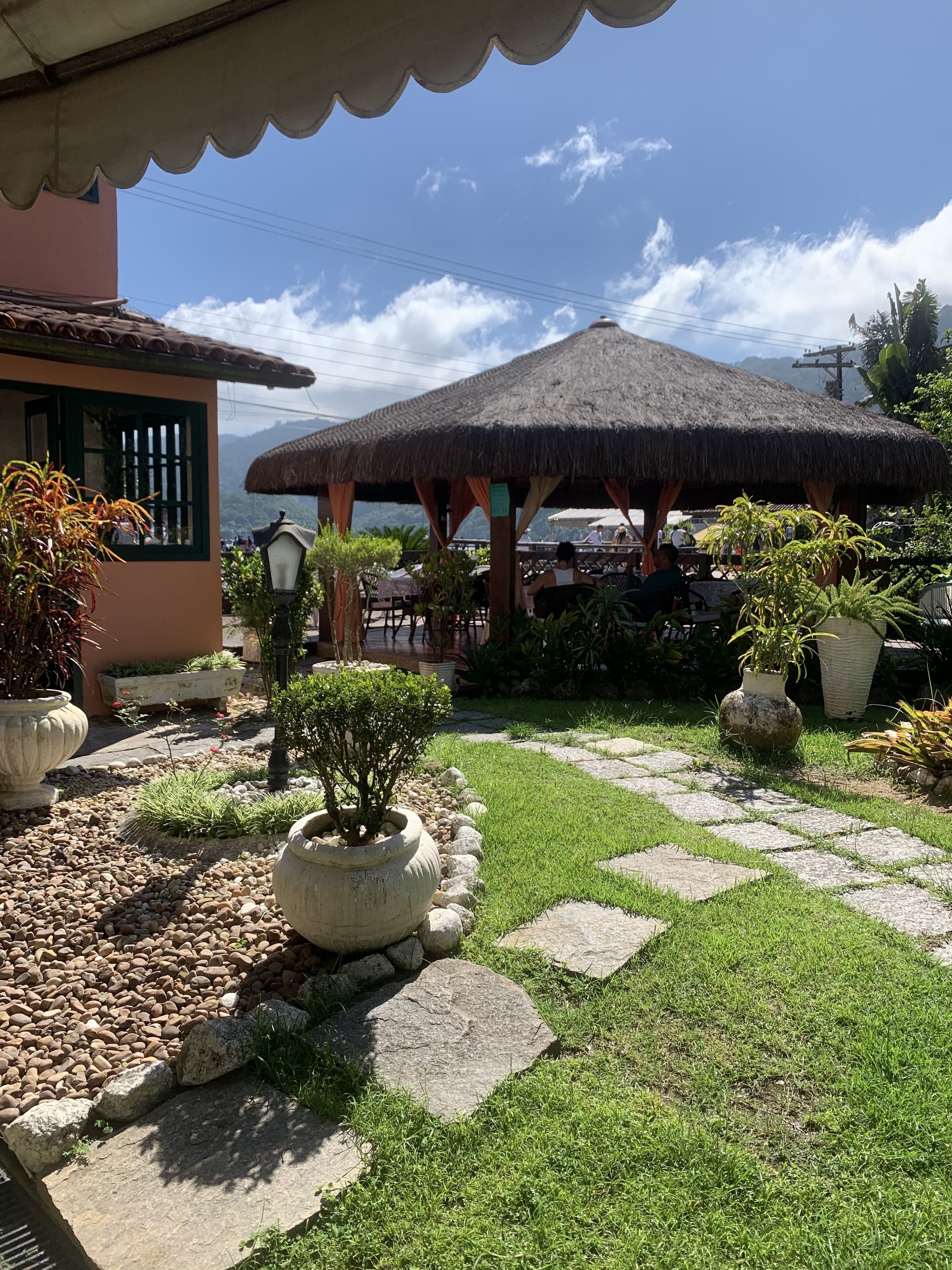 Un patio con un pabellón de techo de paja, plantas en macetas y un camino de piedra.