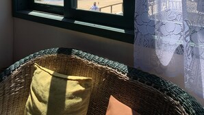 Una habitación con un ventanal grande con vistas a una playa y al agua, una silla de mimbre y una cortina.