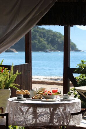 Una mesa dispuesta para el desayuno con vista al mar y una isla boscosa.