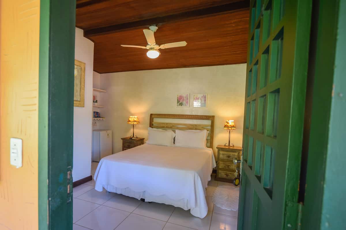 A bedroom with a wooden ceiling, a bed with white bedding, two bedside tables with lamps, and a green door.