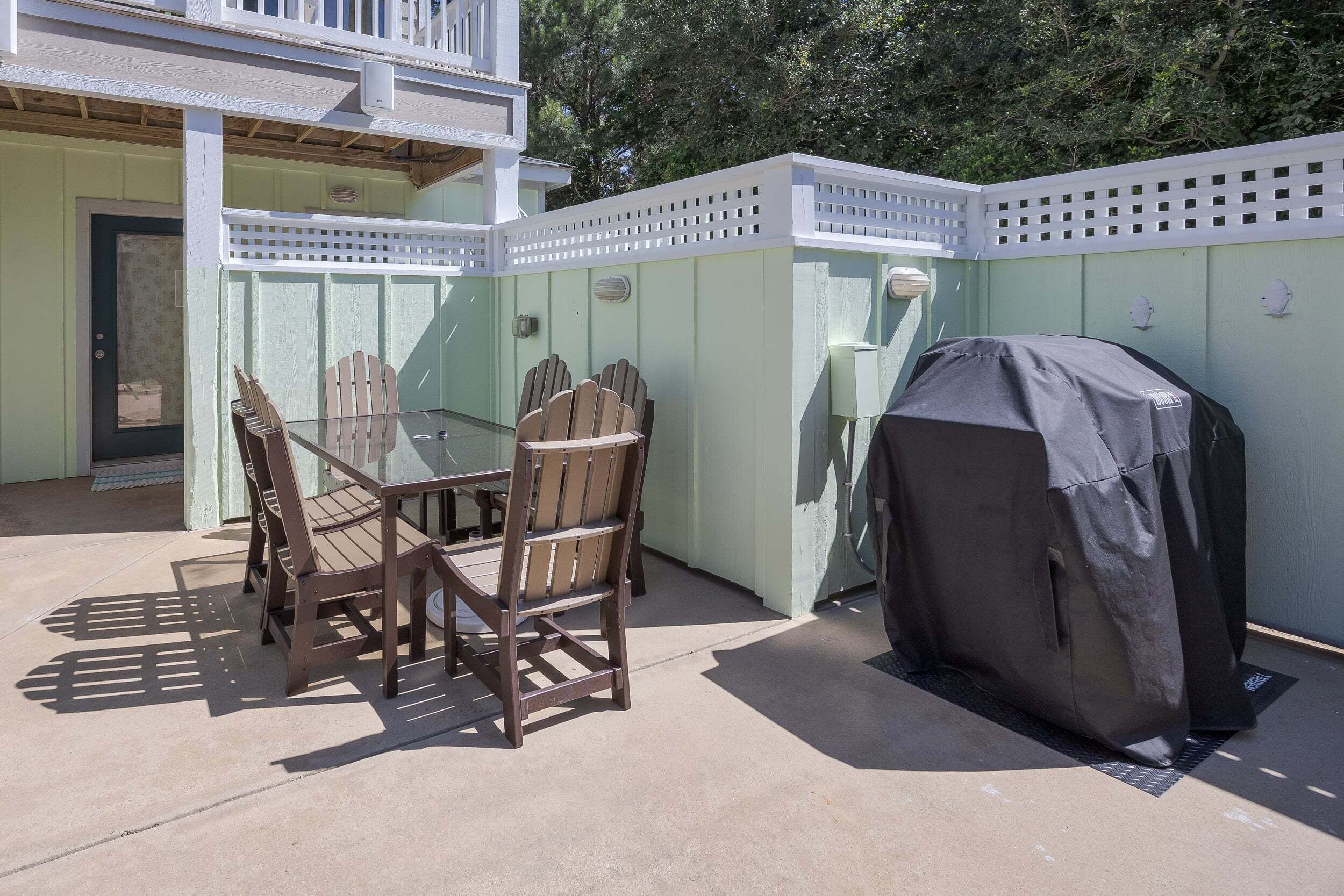 Een terras buiten met een tafel en stoelen, een overdekte barbecue en een witte omheining.