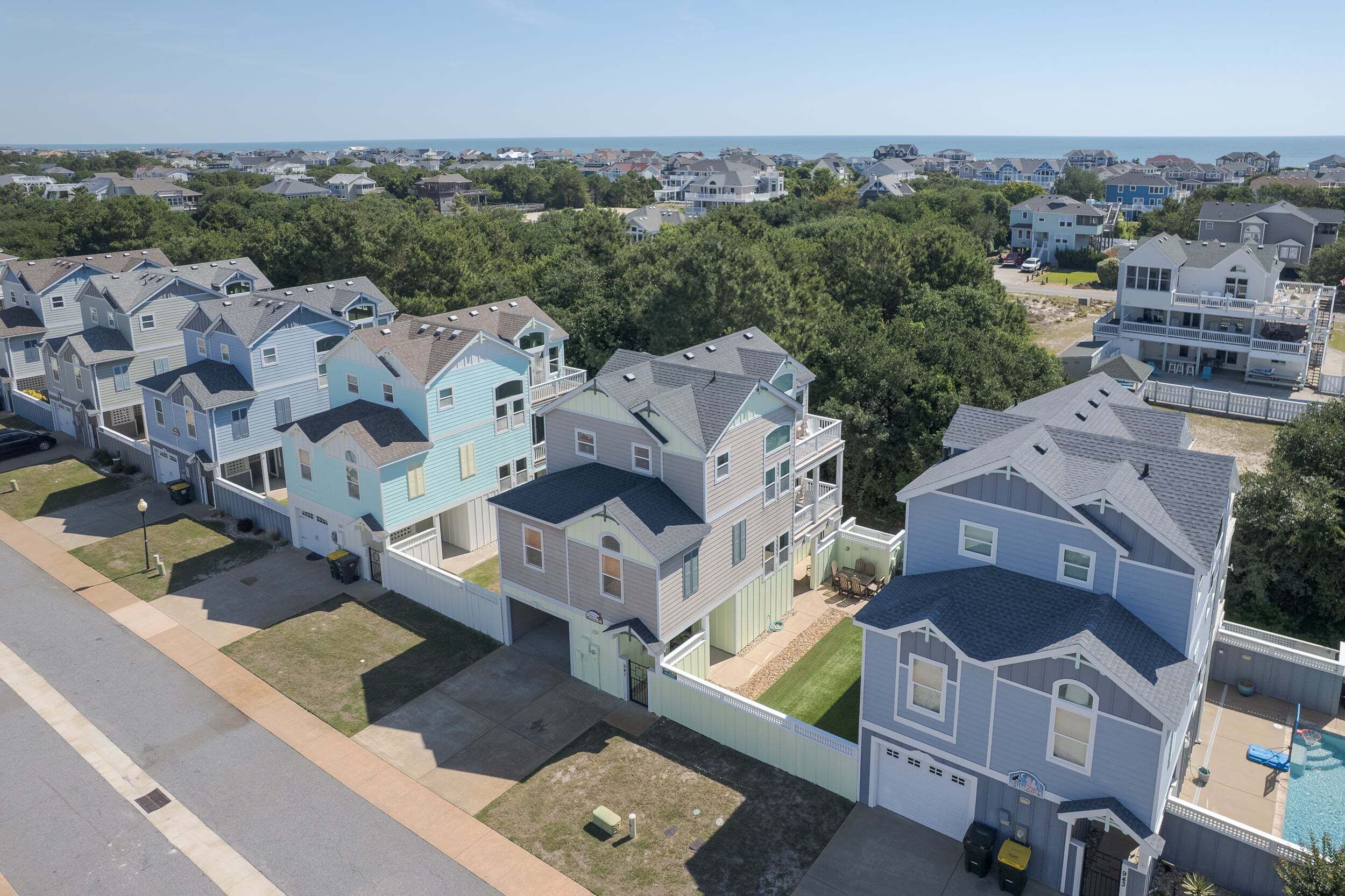 A residential area with multiple two-story houses, a visible swimming pool, and a clear view of the ocean.