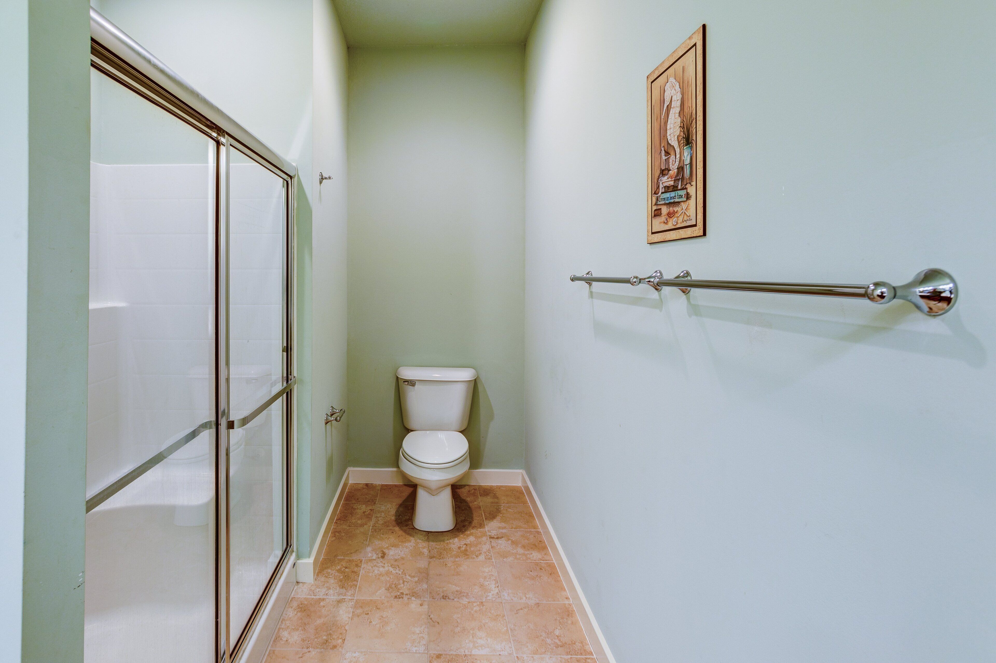 A bathroom with a glass shower enclosure, a toilet, and a handrail.