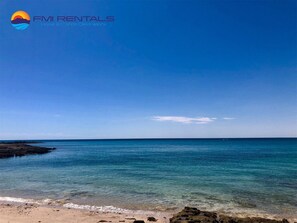 A beach with clear blue water and a rocky shoreline.