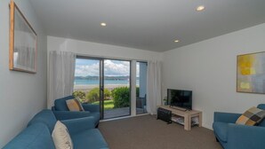Un salón moderno con un ventanal que ofrece vista al mar, un televisor de pantalla plana y dos sofás azules.