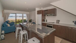 Una cocina moderna con una isla central, un área de comedor con un sofá azul y grandes ventanales con vistas al paisaje.