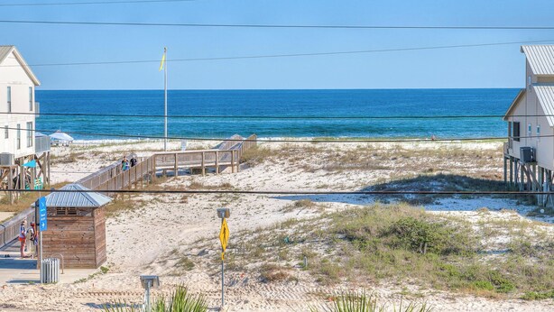 Una propiedad frente a la playa con terraza de madera, un letrero que indica acceso a la playa y vistas al océano.