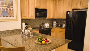 A kitchen with granite countertops, a sink, a microwave, a black refrigerator, and wooden cabinets.