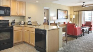 A modern kitchen with granite countertops, wooden cabinets, a black stove, and a dishwasher. There is a dining area with a red upholstered sofa and a small table.