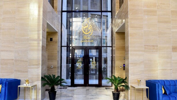 A hotel lobby with marble flooring, a glass entrance, and blue sofas. - Rihanna Hotel (Salmiya)