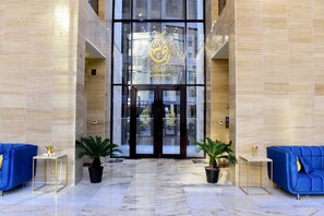 Un vestíbulo de hotel con piso de mármol, entrada de vidrio y sofás azules.