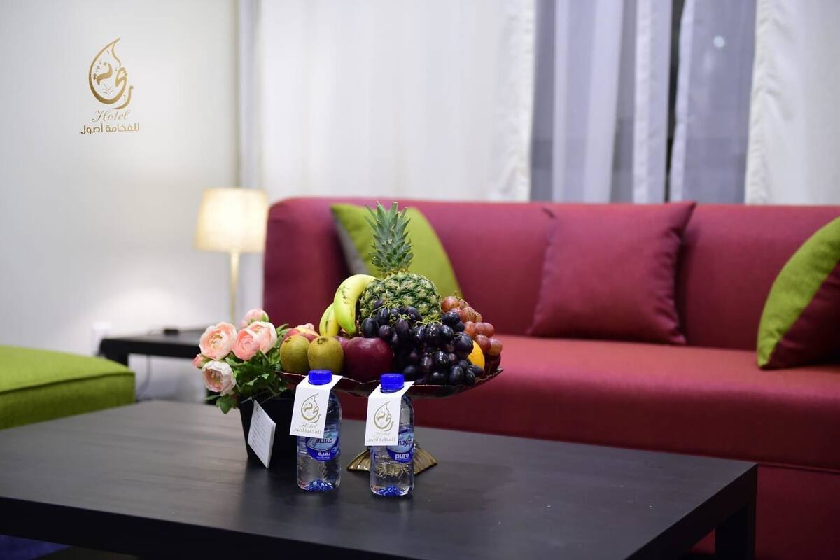 A hotel room with a red sofa, a green armchair, a coffee table with fruit and bottled water.