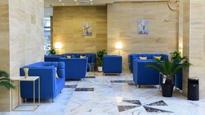 A lobby with blue sofas, marble flooring, and wall art. - Rihanna Hotel (Salmiya)