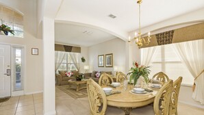 A dining area with a round table, chairs, and a chandelier. There is a living room in the background with a sofa and a coffee table. - Palm Key Villa by VillaDirect (Kissimmee)