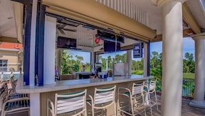 An outdoor bar area with a counter, bar stools, and a view of the surrounding greenery. - Palm Key Villa by VillaDirect (Kissimmee)