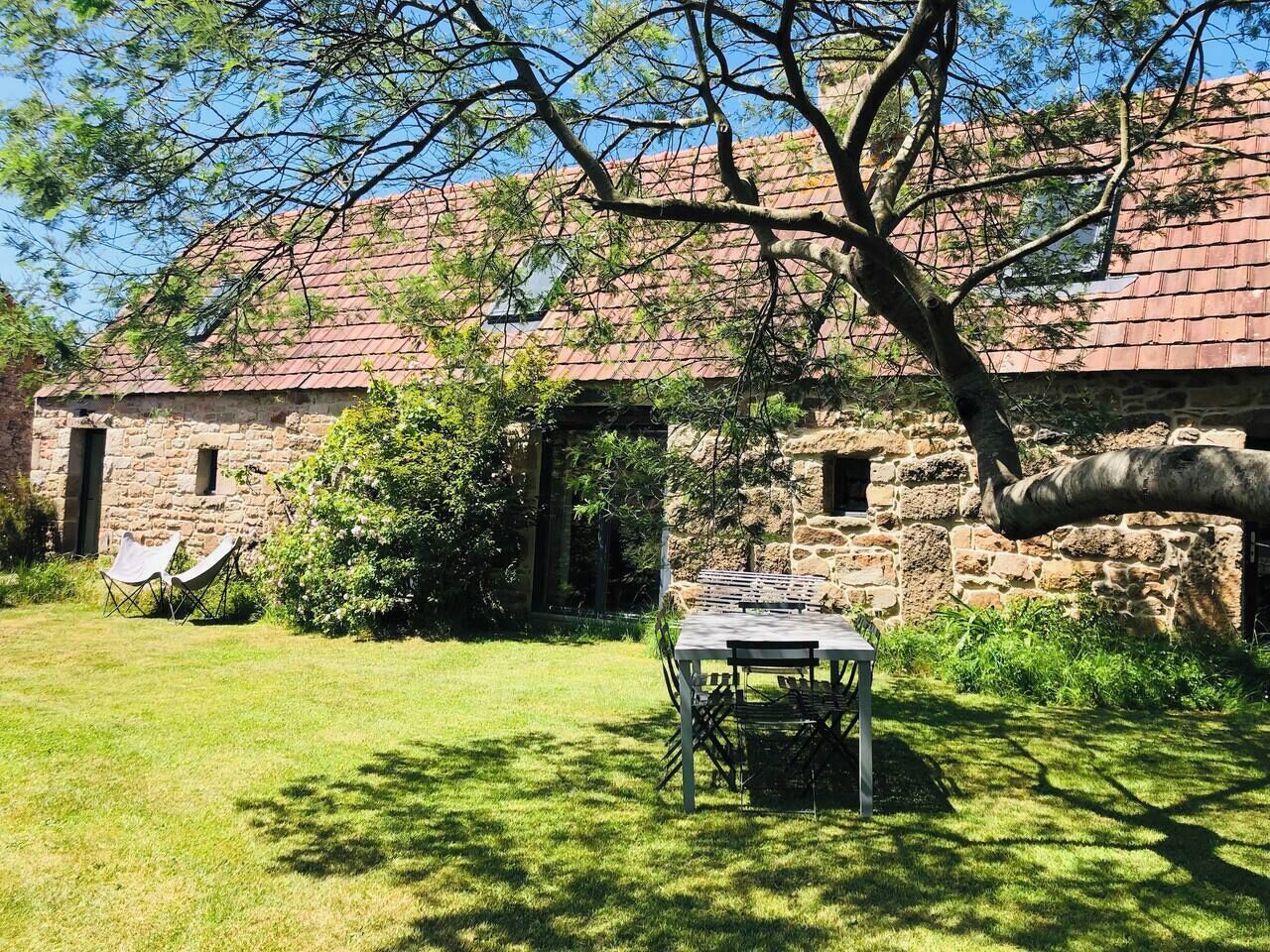 A stone building with a tiled roof, a grassy yard, and a table with chairs.