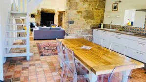Uma cozinha ampla com uma mesa e cadeiras de madeira, uma parede de pedra e uma escada que leva a outro cômodo.