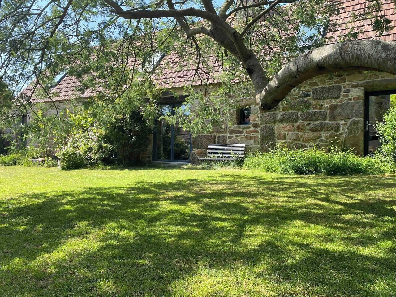 A stone building with a red-tiled roof, a grassy lawn, and a bench.