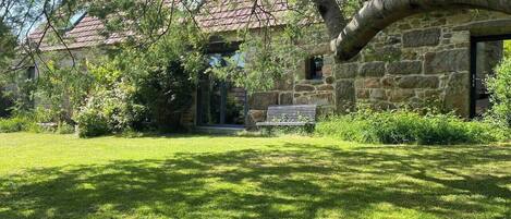 A stone building with a red-tiled roof, a grassy lawn, and a bench.