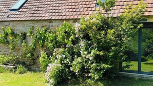 Um edifício de pedra com telhado de telhas vermelhas, uma pequena janela e um jardim com plantas floridas.