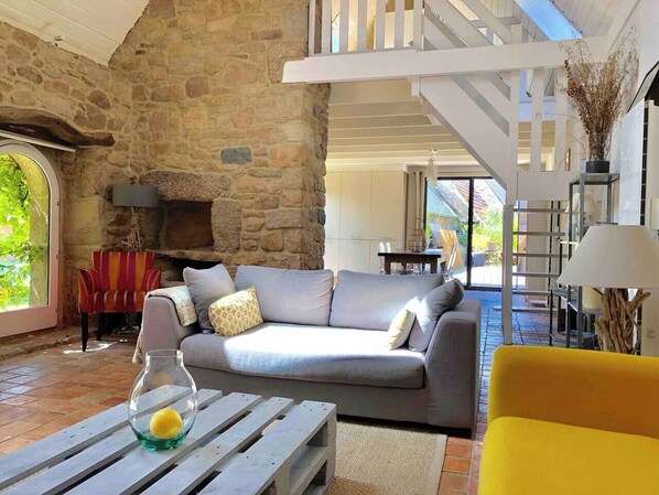 A cozy living room with a stone wall, a grey sofa, a yellow armchair, and a wooden coffee table with a glass vase.