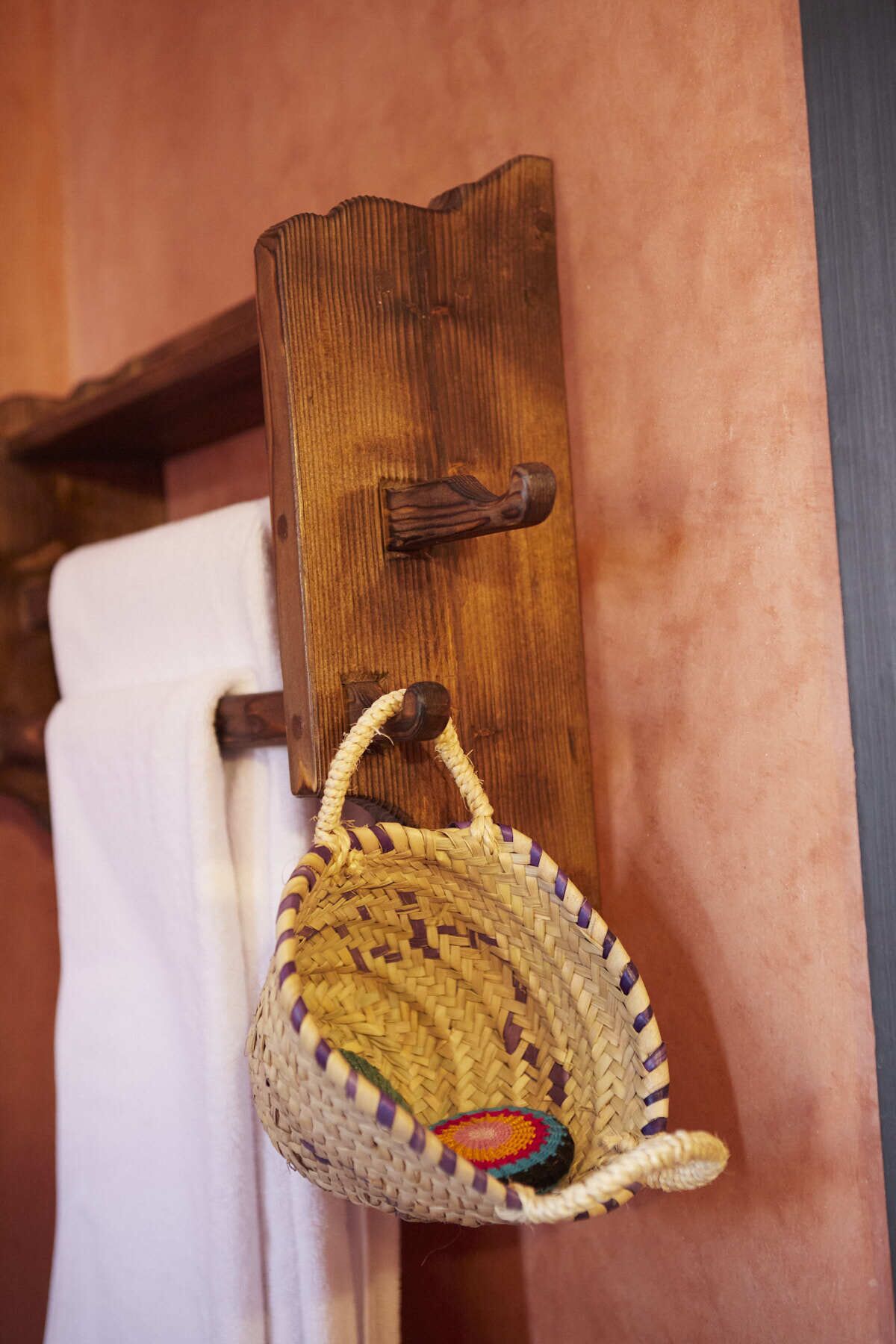 Una cesta tejida colgada en un soporte de madera en la pared, con una toalla colgando debajo.