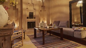A cozy living room with a fireplace, a sofa, a coffee table, and a dining table. - Kasbah Flilou (Ait Sedrate Jbel El Soufla)