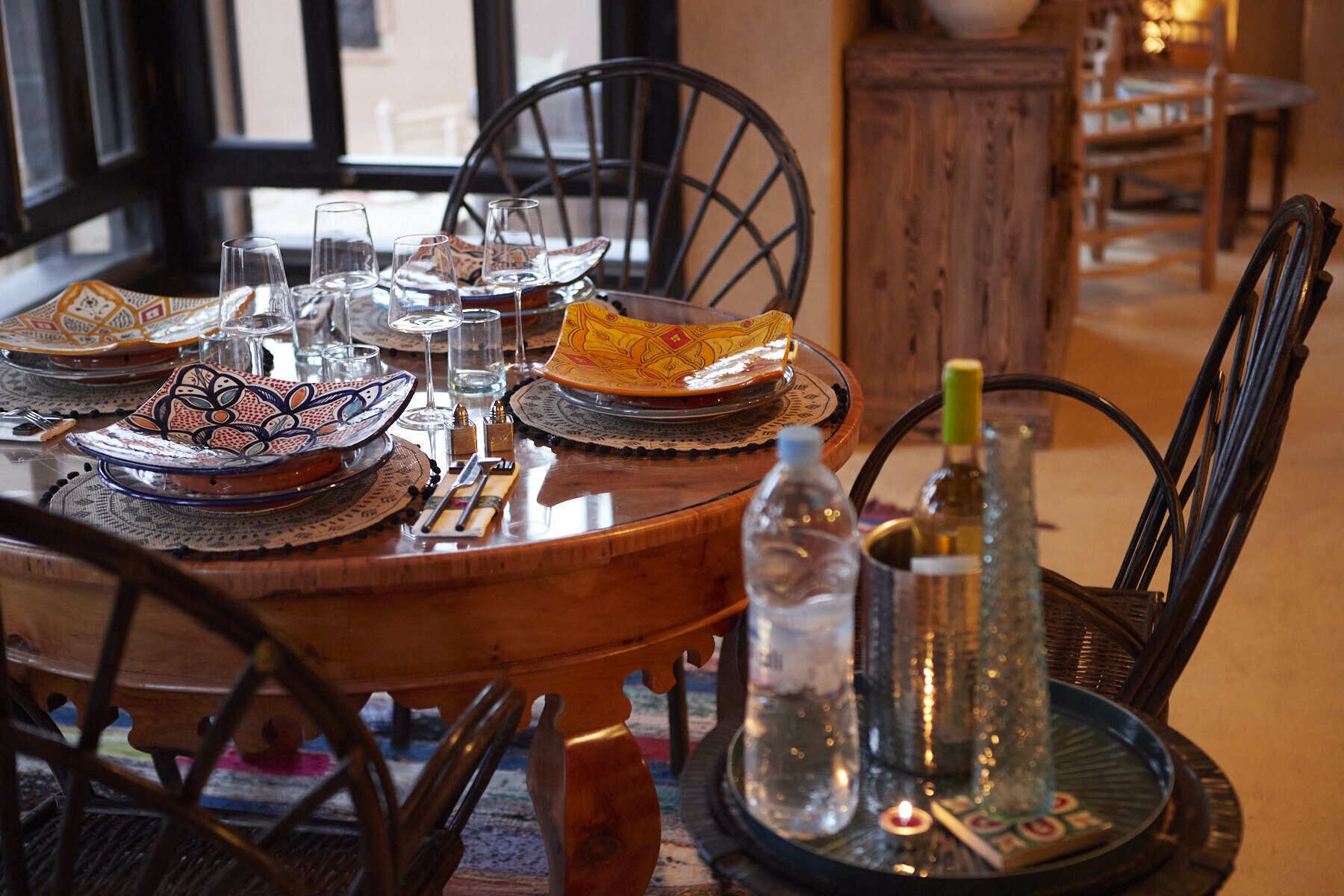 Una mesa de comedor dispuesta con platos tradicionales marroquíes, vasos y una botella de agua.