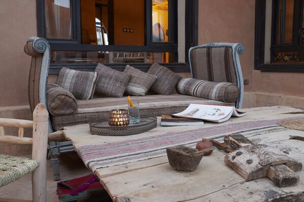 Un rincón exterior acogedor con un sofá, cojines, una mesa de fibra natural y un cuenco decorativo.