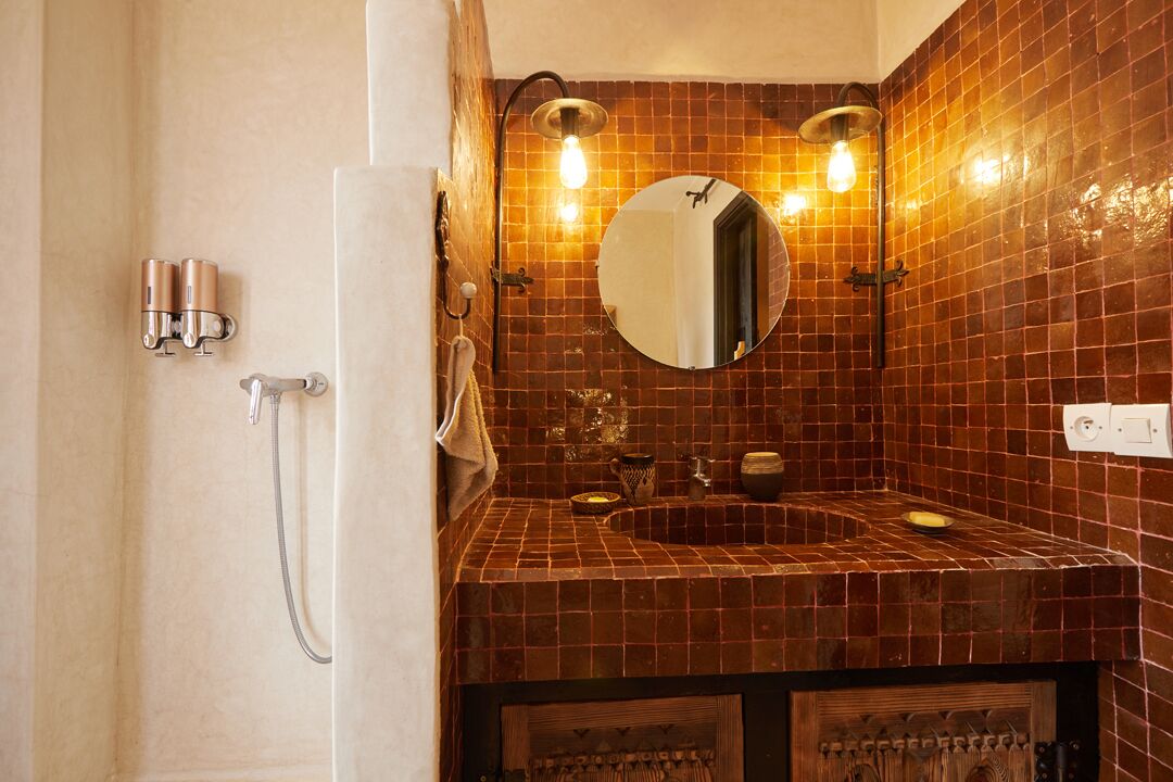 A bathroom with a tiled wall, a round mirror, a sink, and a shower.