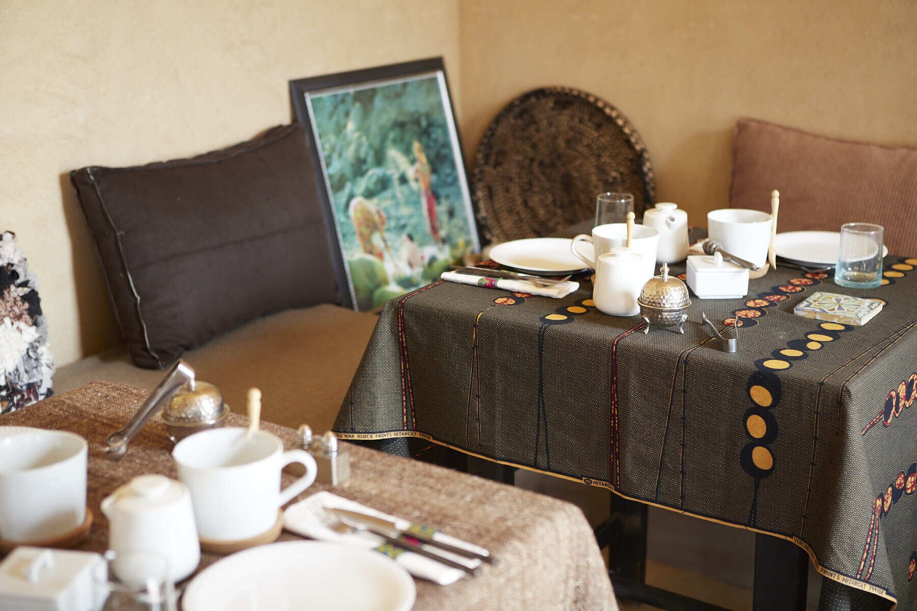 A dining table set with white dishes, cups, and cutlery, a small decorative item, and a framed picture on the wall.