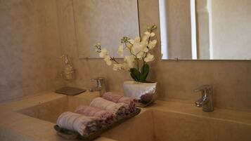 A bathroom with a beige sink, two faucets, a soap dispenser, and a potted orchid.