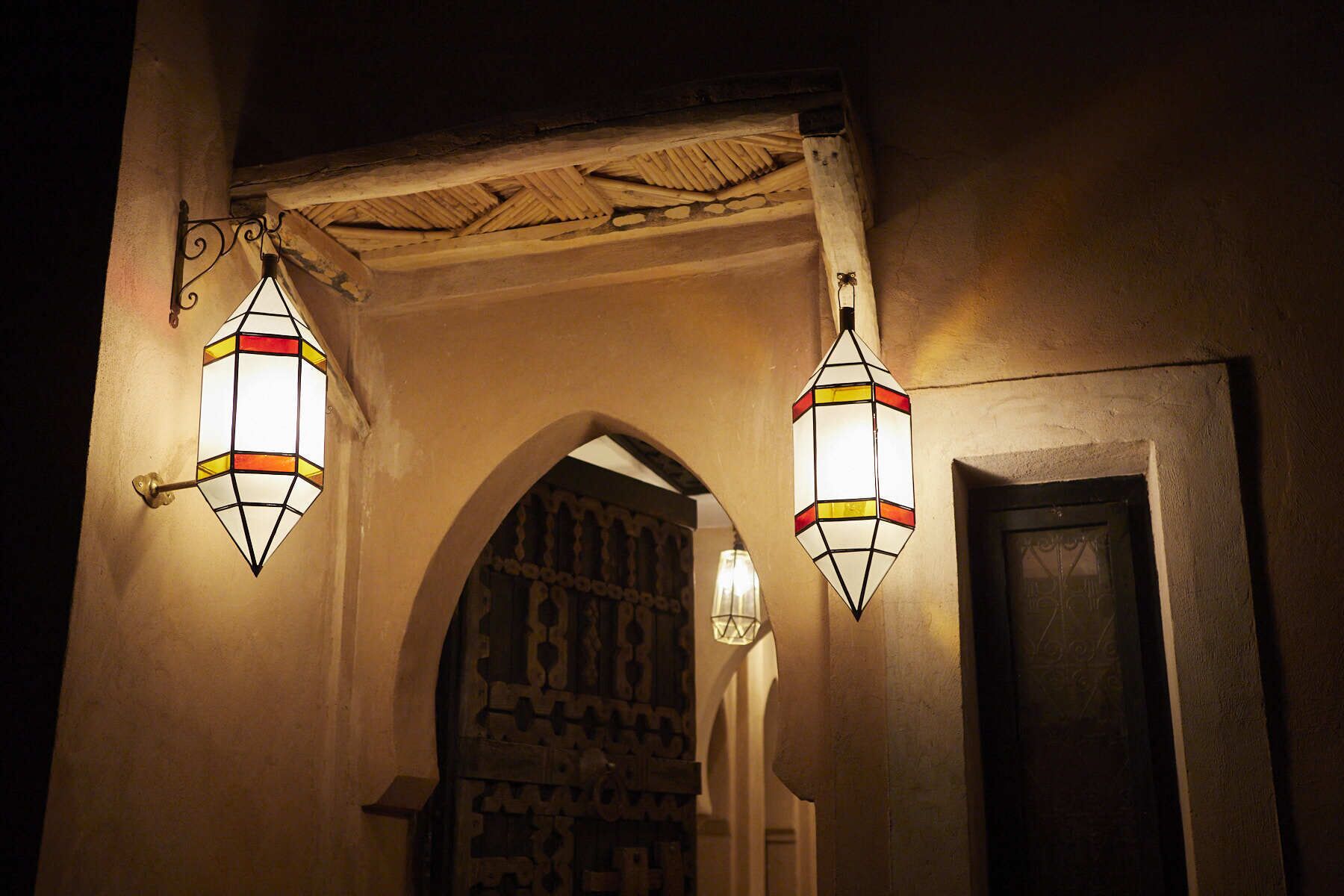 A hallway with two hanging lanterns, an arched doorway, and a door.