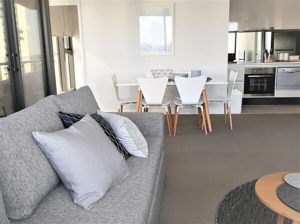 A modern living room with a grey sofa, white chairs, a dining table, and a kitchen area with appliances. - Central Location & WiFi (Melbourne)
