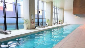 Una piscina interior con agua cristalina, suelo de baldosas y tumbonas a un lado.