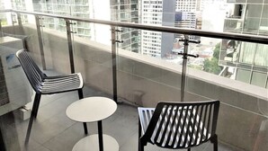 Un balcón con dos sillas y una mesita, con vistas a un paisaje urbano de edificios altos.