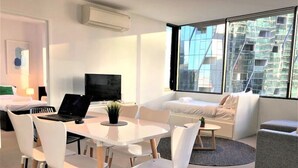 Habitación de hotel moderna con zona de comedor, sofá y vistas a un edificio.