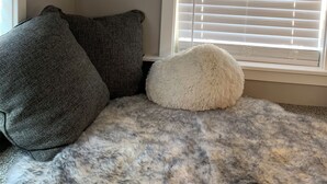 Une pièce avec une fenêtre, un oreiller blanc moelleux et deux oreillers gris foncé posés sur un tapis à motifs.