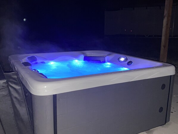 A hot tub with blue lighting, surrounded by a dark outdoor setting.