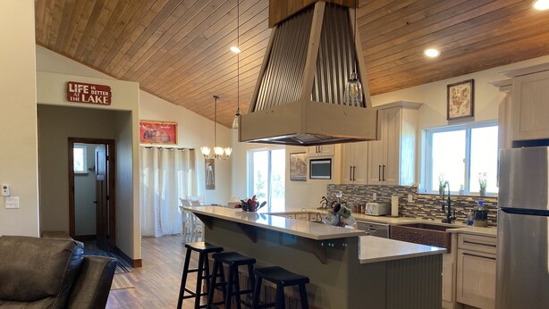 A modern kitchen with a central island, bar stools, wooden flooring, and a view of the outdoors. - Mountain Meadow, 3-bedroom vacation home, close to RMNP & lakes, Hot tub, W/D (Grand Lake)