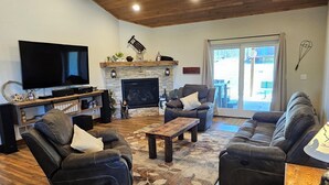 Ein geräumiges Wohnzimmer mit Holzbalkendecke, Kamin, Flachbildfernseher und bequemen Sitzmöglichkeiten.