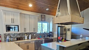 A modern kitchen with wooden flooring, white cabinetry, a central island, and a large range hood. - Mountain Meadow, 3-bedroom vacation home, close to RMNP & lakes, Hot tub, W/D (Grand Lake)