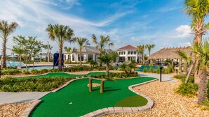 Un campo de golf con un putting green, palmeras y un edificio con techo rojo.