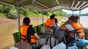 Ein Boot mit Passagieren in Rettungswesten, ein Fluss und grüne Vegetation im Hintergrund.