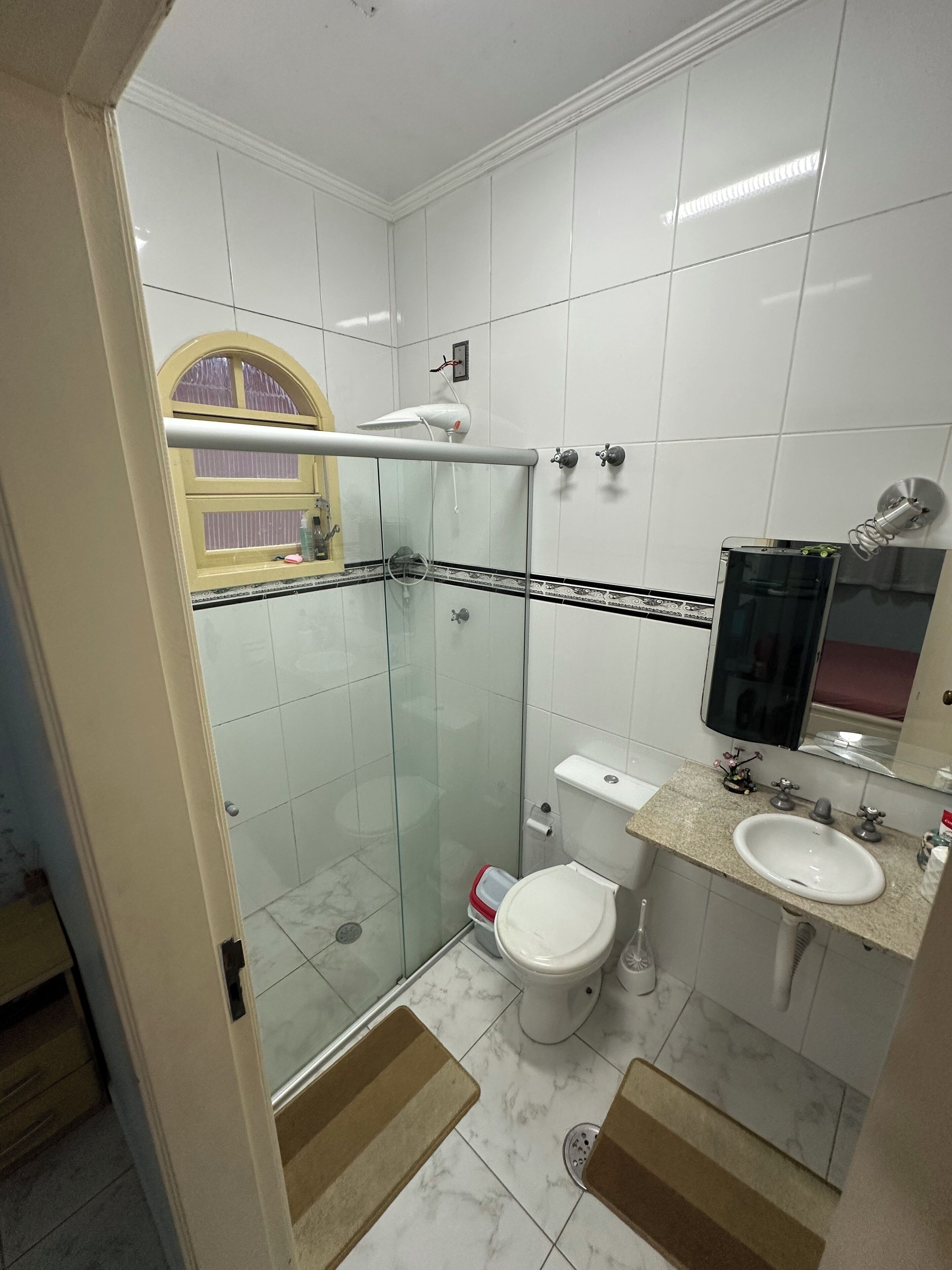 Un bagno con box doccia in vetro, un water, un lavandino e uno specchio.