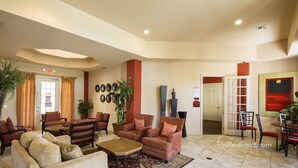 A spacious lobby with multiple seating areas, including sofas and armchairs, a coffee table, and a patterned rug. There is a reception desk, a plant, and a door leading to other areas. - Cresent Moon by VillaDirect (Davenport)
