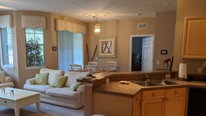A living room with a sofa, coffee table, and a kitchen area with a sink and cabinets. - Cresent Moon by VillaDirect (Davenport)