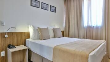 A hotel room with a bed, bedside table, and a telephone. There are three framed pictures on the wall.